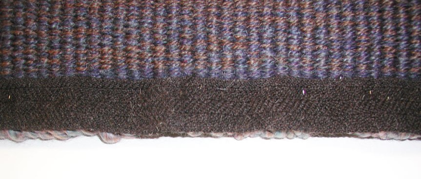 Photo of handspun handwoven twill fabric pinned to the edge of a handwoven rug to test it as a possible finishing technique. fabric